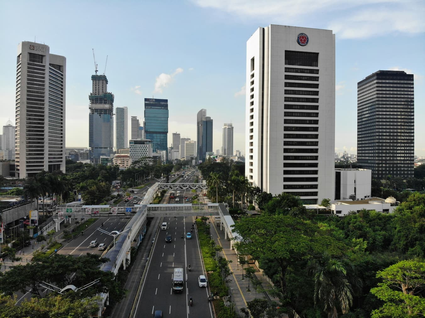 Jakarta city skyline with modern office towers, busy urban highway and surrounding greenery.